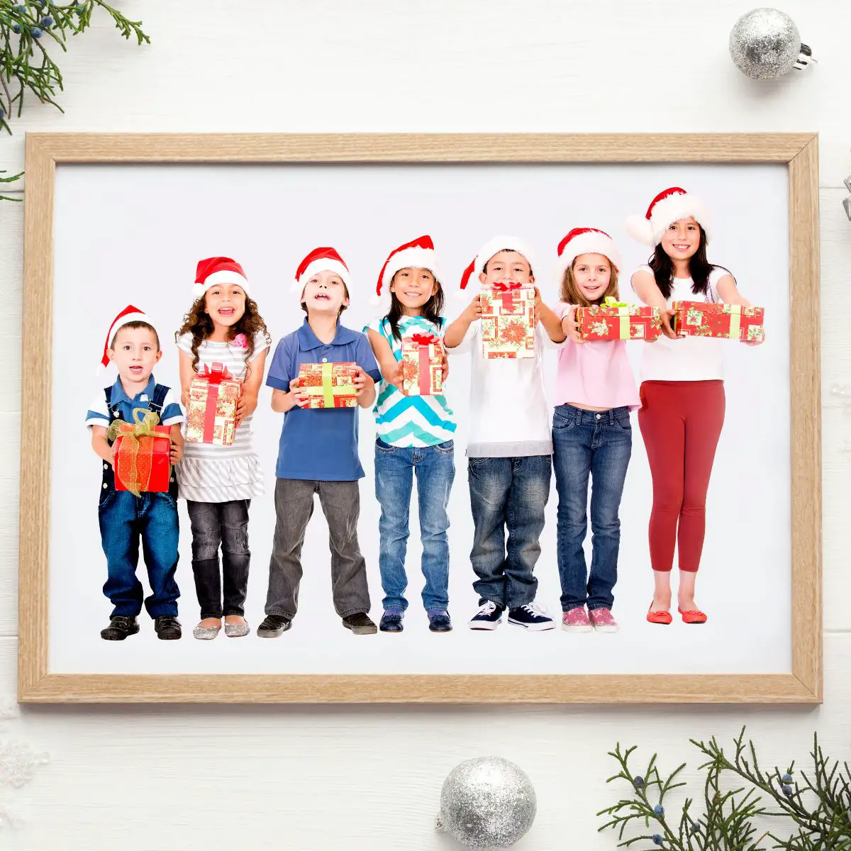 Hellbrauner Bilderrahmen auf weißem Hintergrund. In dem Bilderrahmen sind verschieden große Kinder im Grundschulalter zu sehen. Der Bilderrahmen liegt auf einem weihnachtlich geschmückten Tisch.